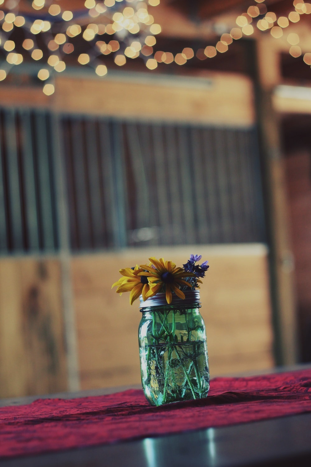 A mason jar of sunflowers on a table under string lights
